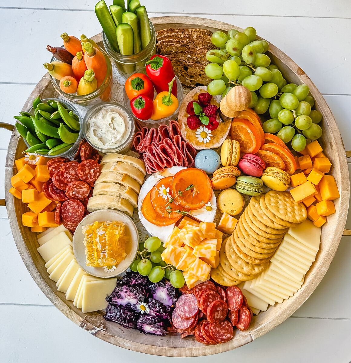 Round charcuterie committee  with meats, cheese, crackers, and different   colorful snacks