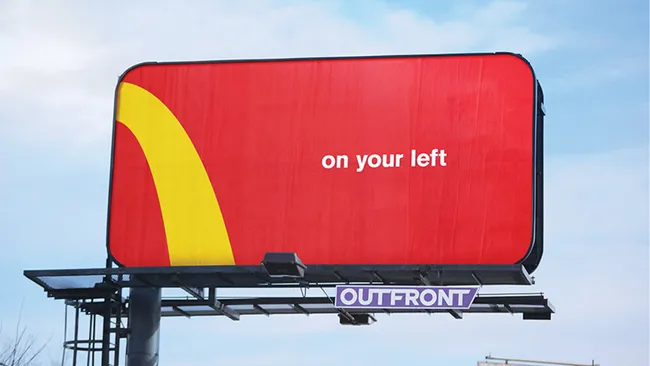 A reddish  and yellowish  McDonald's billboard advertisement  showing the elemental  substance   "on your left".