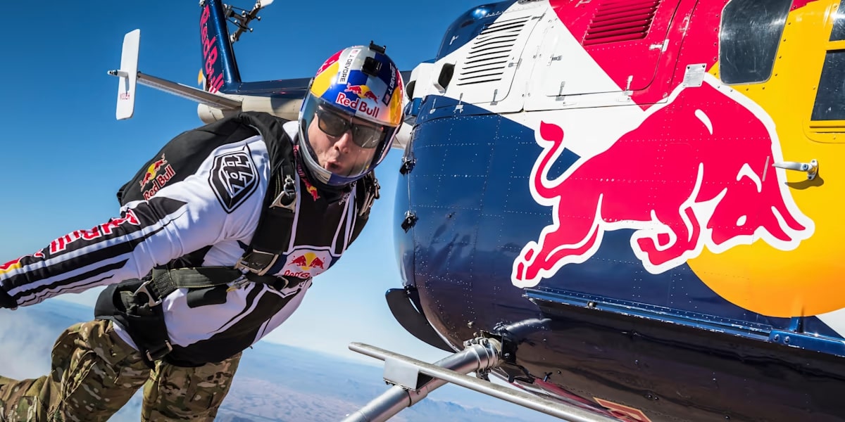 A paraglider wearing Red Bull branded equipment next to branded helicopter