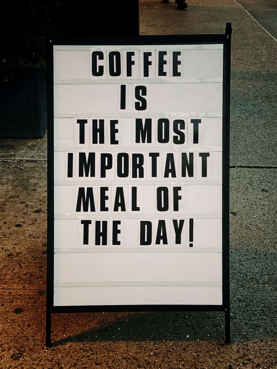 A white board with the quote ‘Coffee is the most important meal of the day’ in black letters