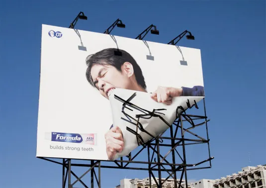 A billboard ad that says "building strong teeth" showing a man ripping the corner of the billboard with his teeth.