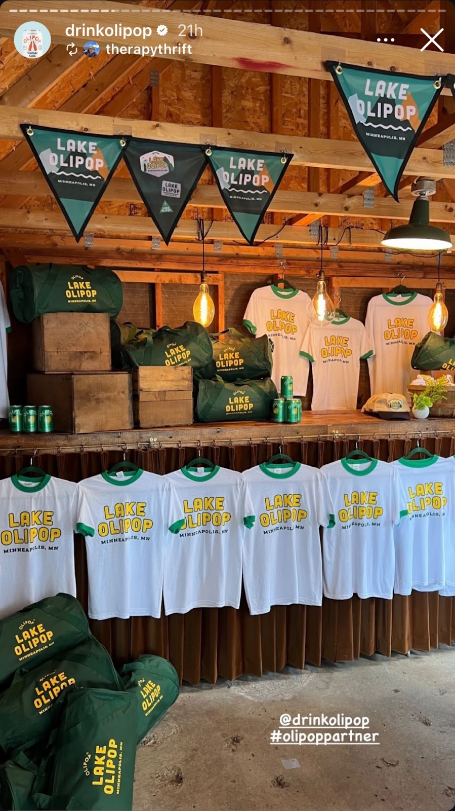 Instagram story showing rustic display of "Lake Olipop" merchandise with banners, duffel bags, T-shirts, cans