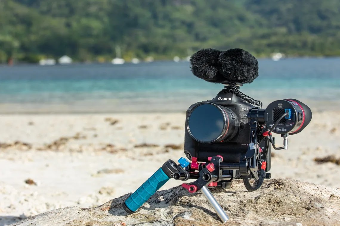 A picture of a camera laying on the sand, with sea in the background bu Canon